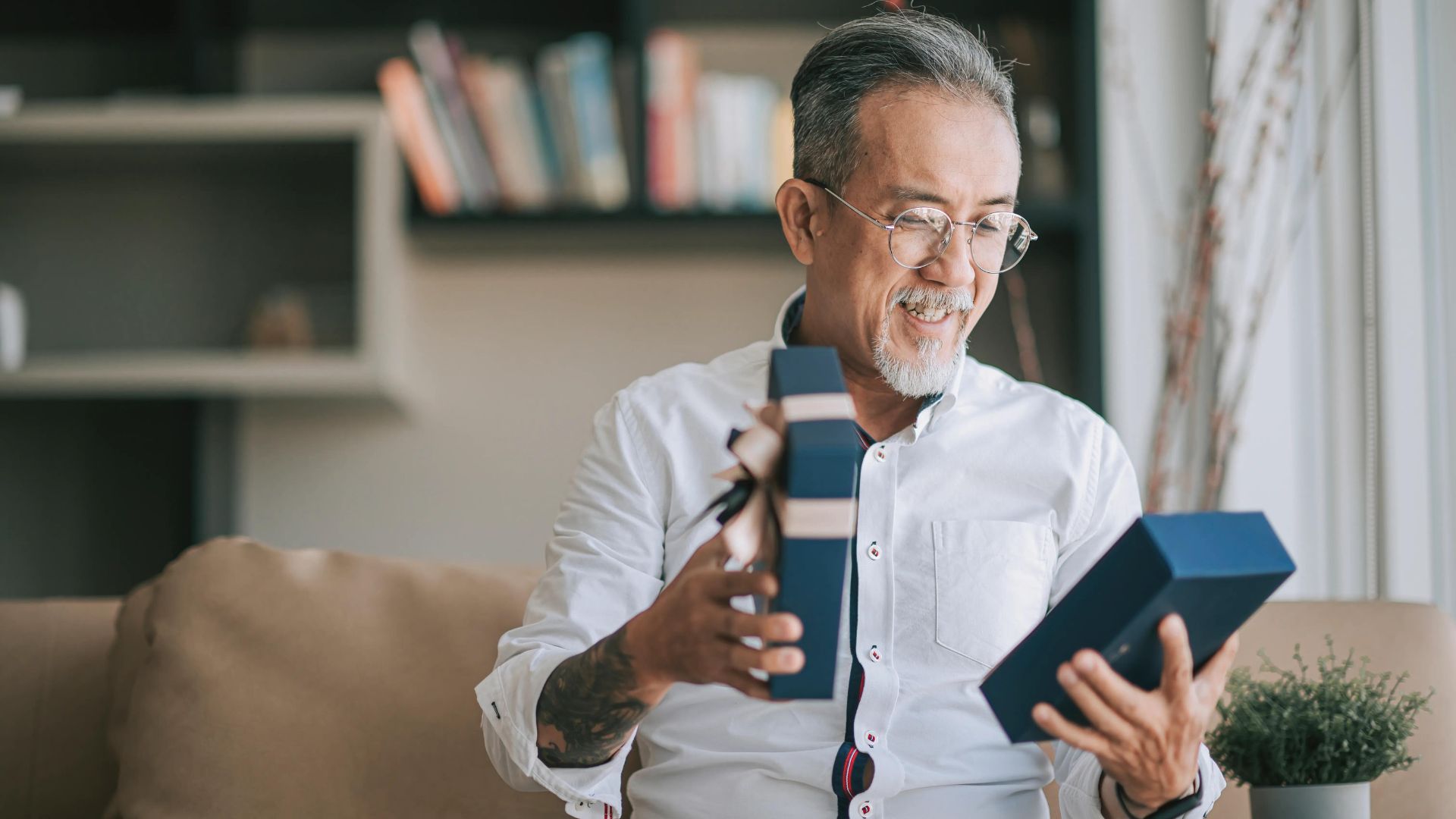 a man wearing glasses while opening a box of gifts showing one of things what most men want for father's day